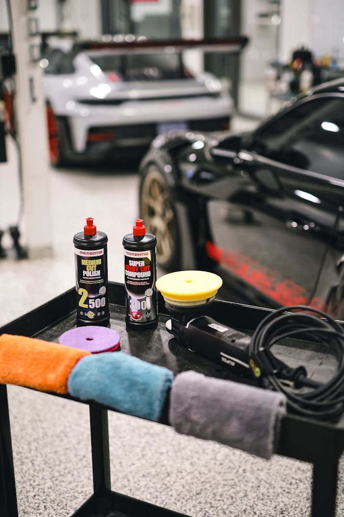 Car detailing products and equipment on table in modern garage with sports cars.