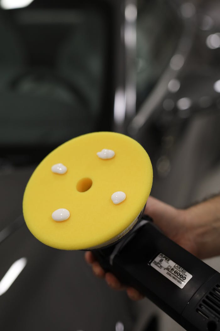 Professional car detailing with a polisher and cream for a glossy finish.