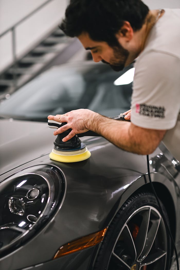 Experienced technician polishing a sleek sports car using a buffer for optimal shine.